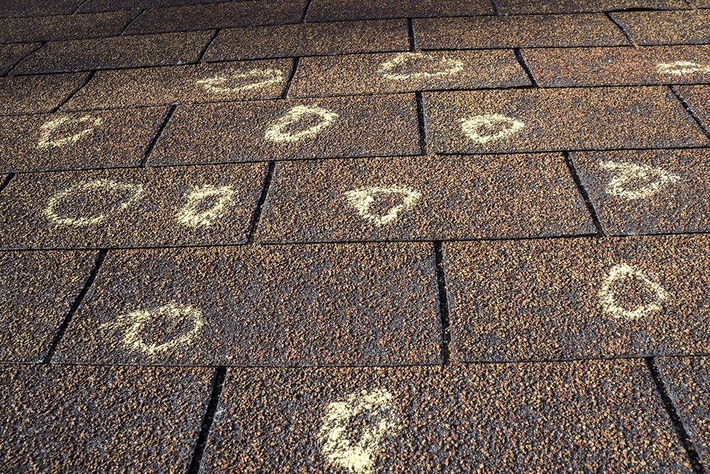 Roof shingles with multiple chalk circles highlighting potential damage areas.