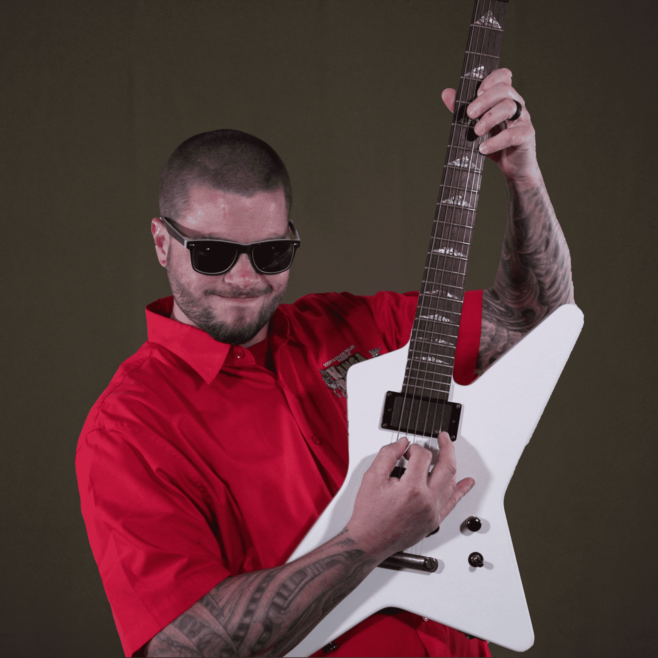 A person in a red shirt and sunglasses is playing a white electric guitar against a plain dark background.